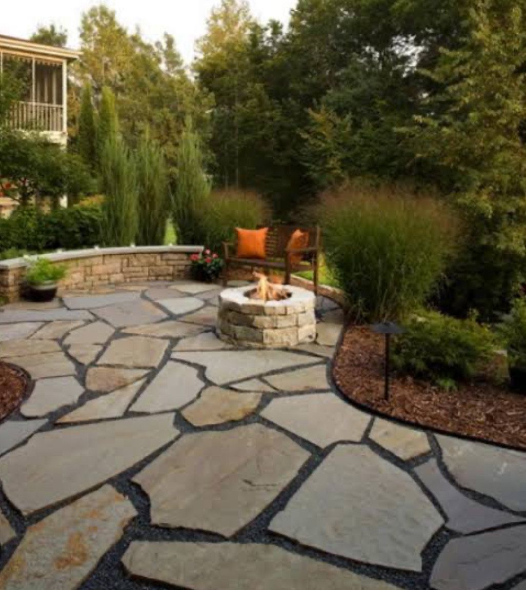 A stone patio with a fire pit and chairs