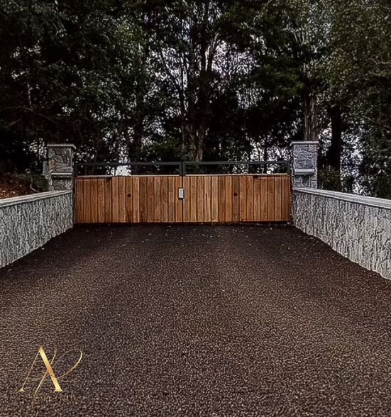 A wooden gate is in the middle of a gravel driveway