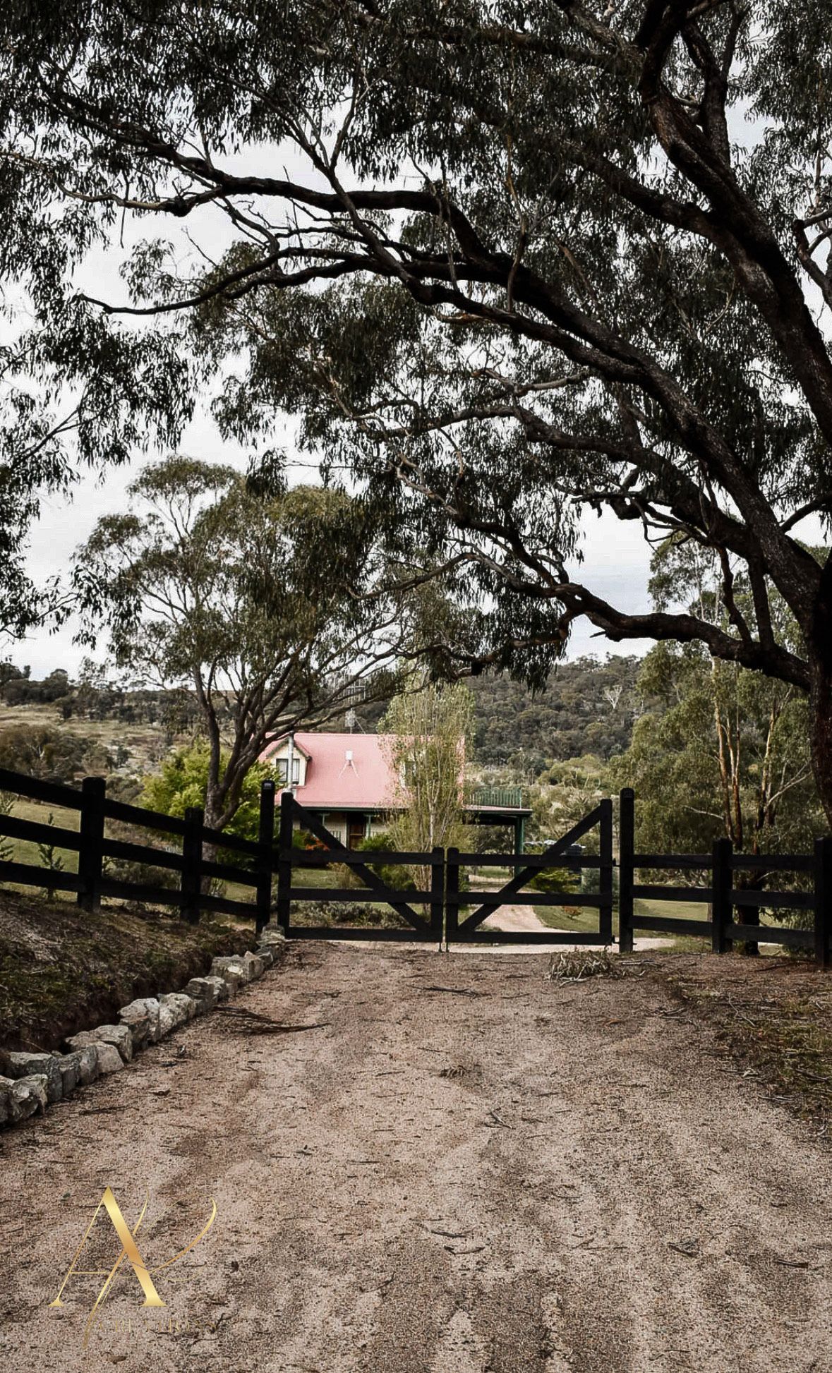 A dirt road with a fence and a gate leading to a house.
