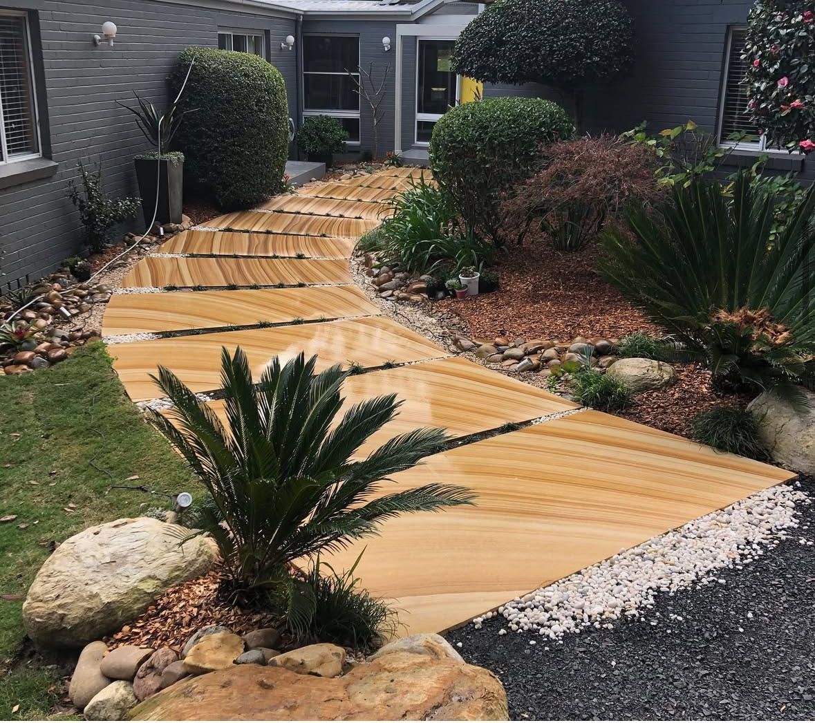 A wooden walkway leading to a house surrounded by plants and rocks