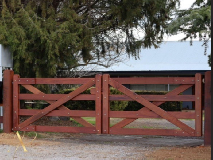 A wooden gate is open to a driveway in front of a house