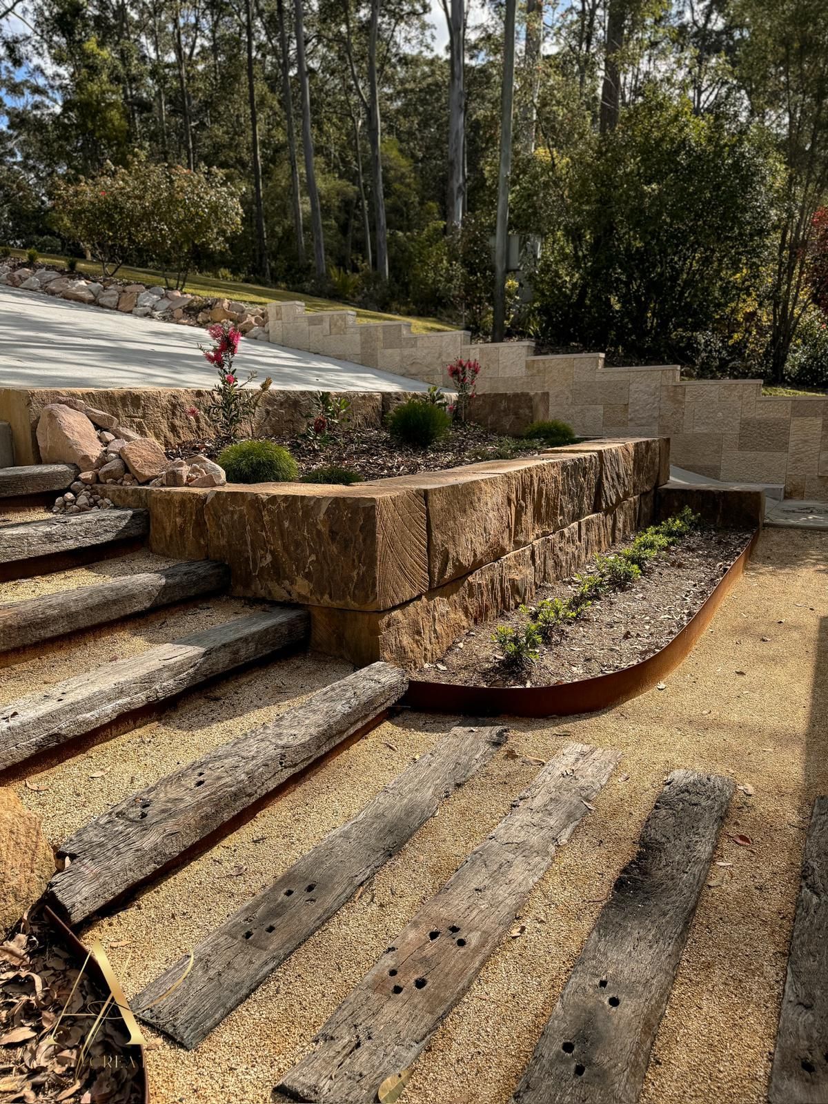 A wooden staircase leading up to a lush green garden with trees in the background.