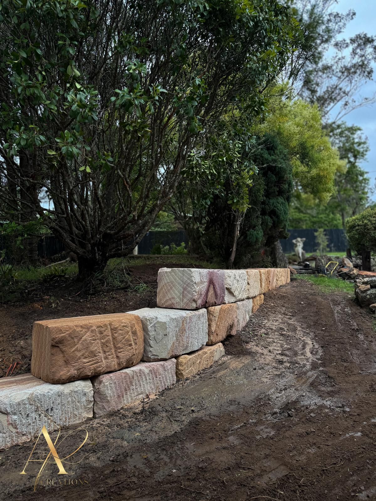 A stone wall is being built in a yard with trees in the background.
