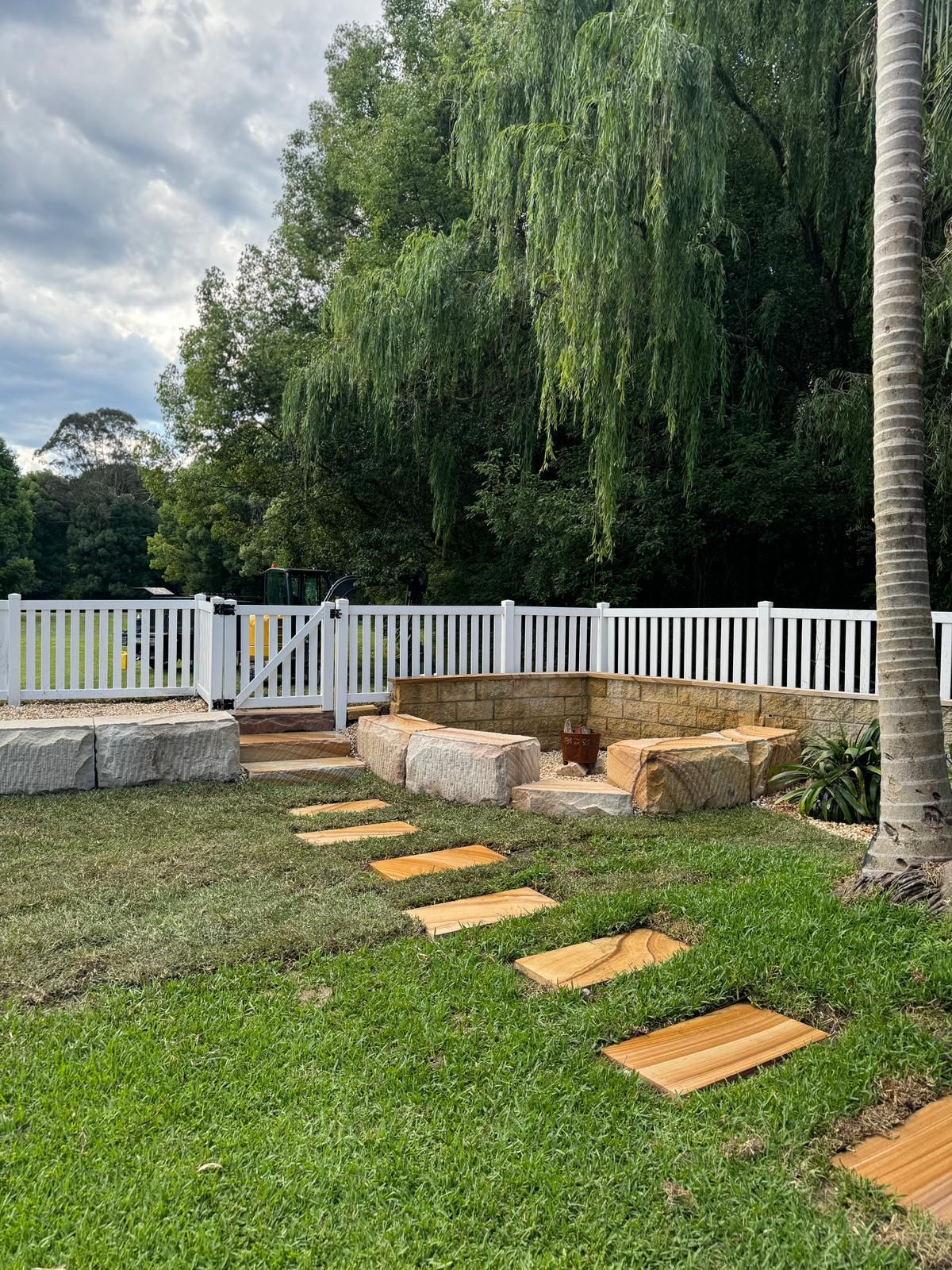 A backyard with a white fence and wooden stepping stones.