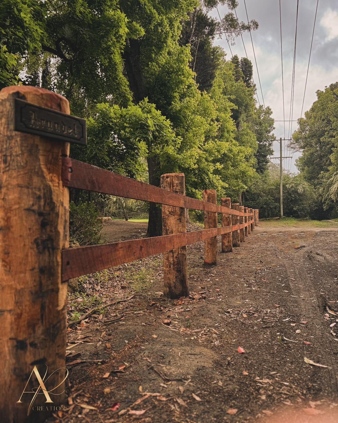 A wooden fence surrounds a dirt road with trees in the background