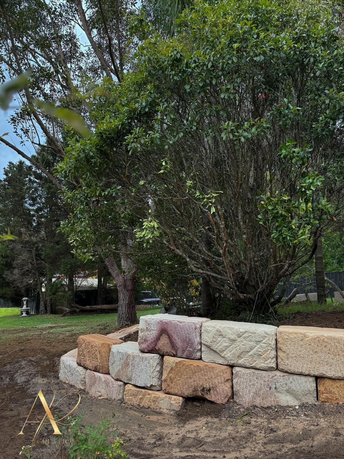 A stone wall is being built in a yard with trees in the background.