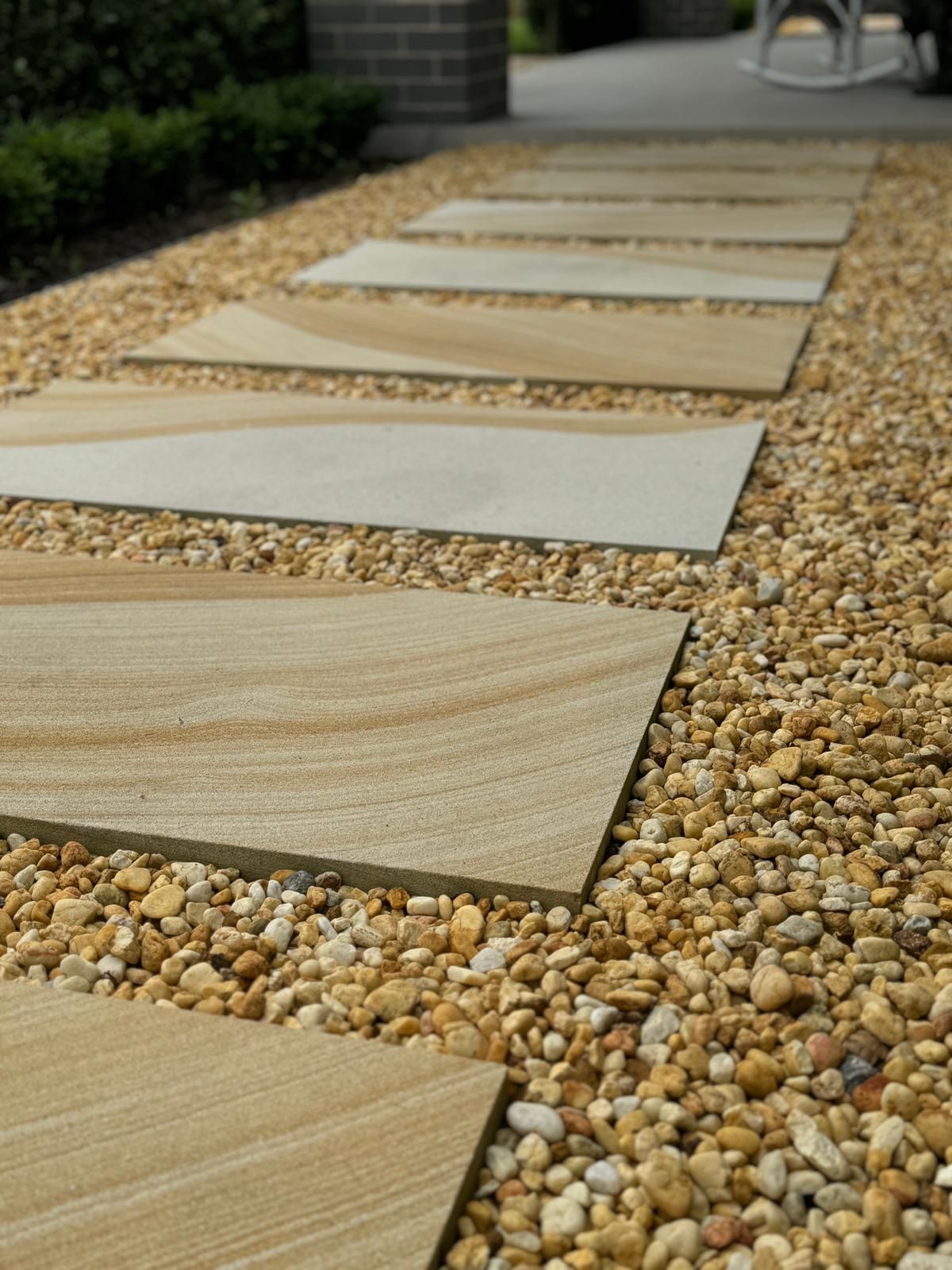 A walkway made of tiles and gravel with a rocking chair in the background