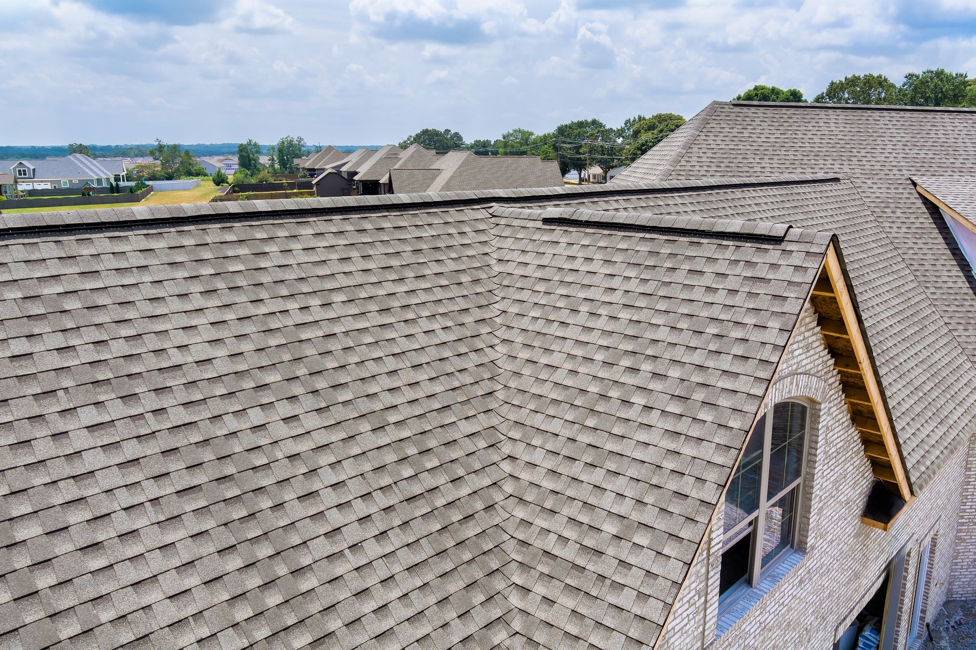 Overhead view of a gray shingle roof on a house, with other houses in the background under a cloudy sky.