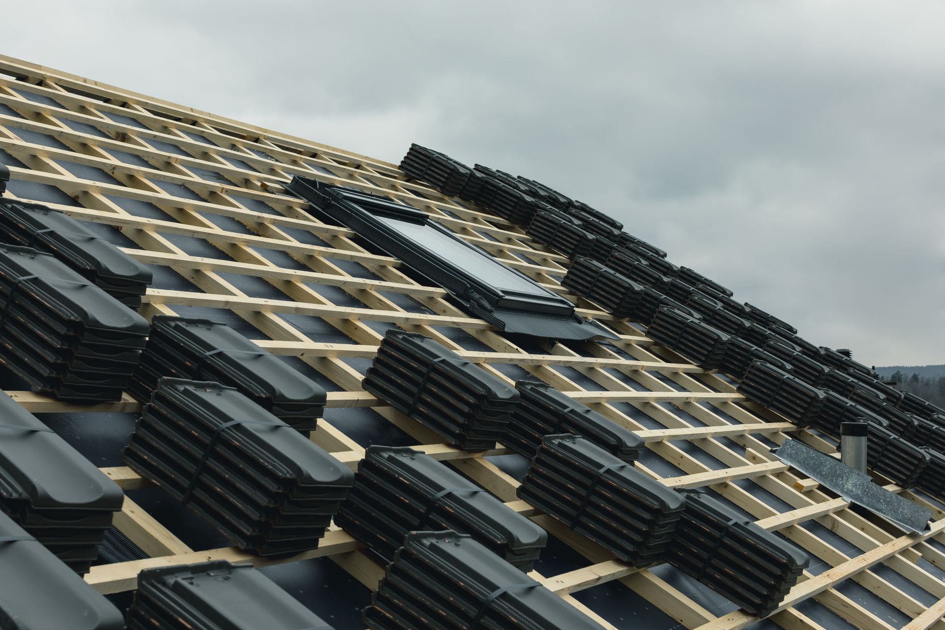 Rooftop under construction; dark roofing tiles stacked on wooden supports.