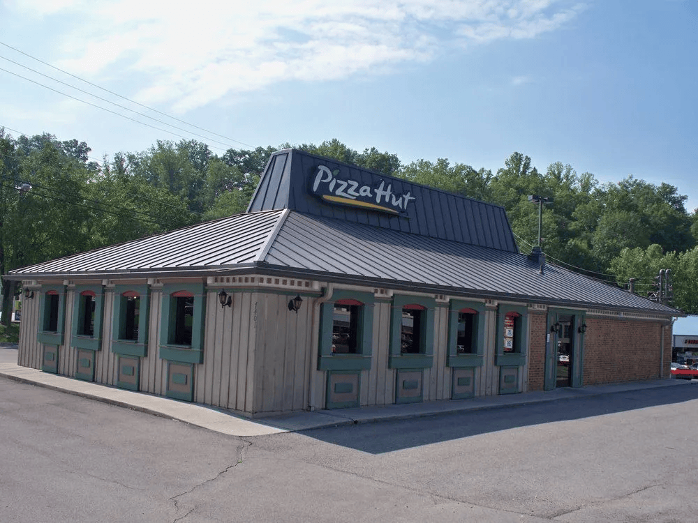 Pizza Hut restaurant with a gray roof and light brown siding, windows with green shutters.