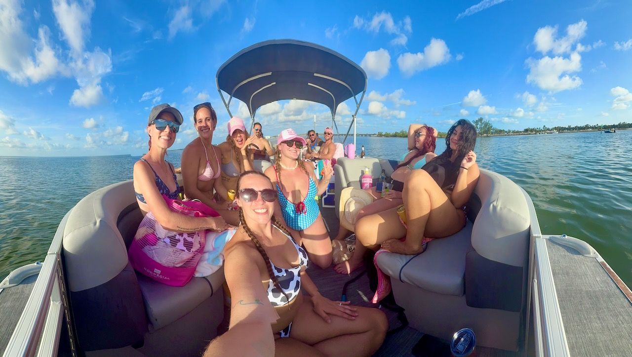 Group of people waving from a pontoon boat on a sunny day at sea.
