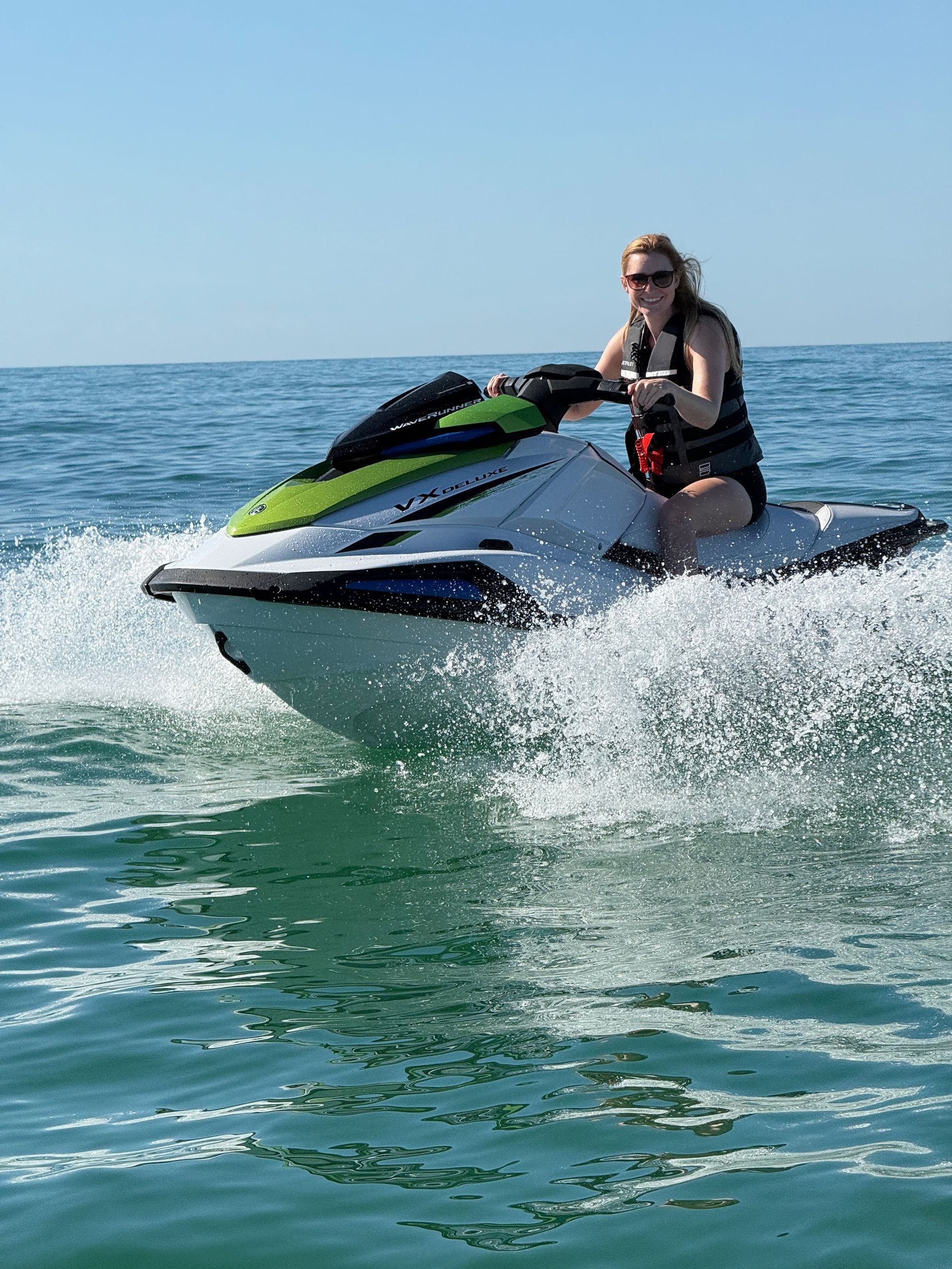 Two people ride a blue jet ski on turquoise water; sunny day.