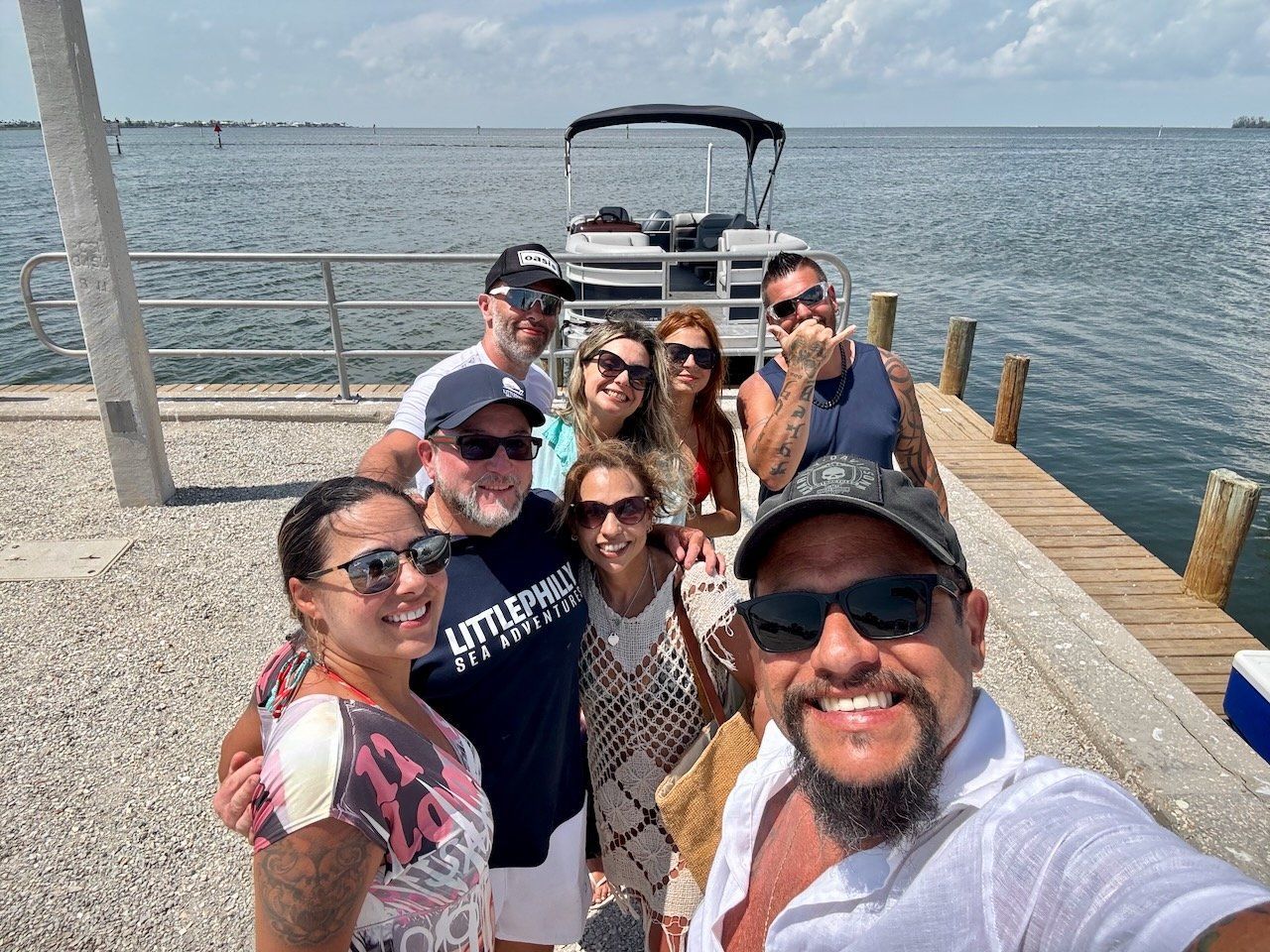 Group of people on a wooden dock with a boat in the background, posing for a photo on a sunny day.