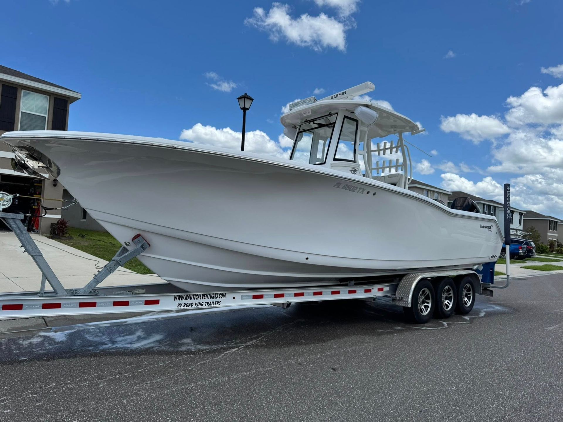 White boat on a trailer in a suburban street on a sunny day.