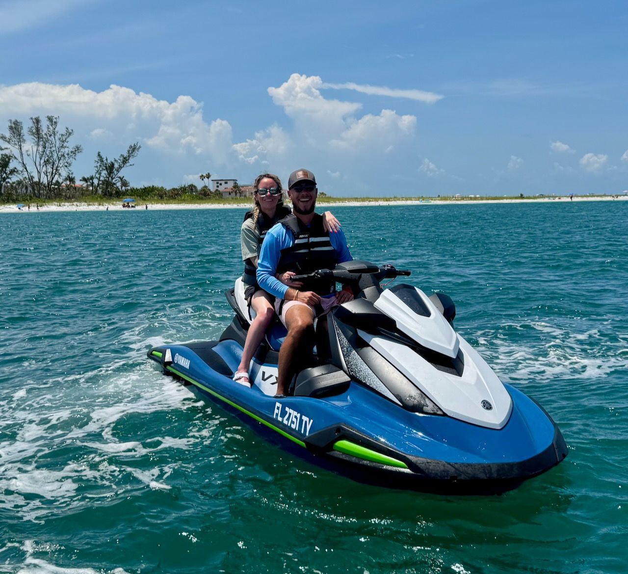Couple on a blue jet ski in the ocean under a bright sky.