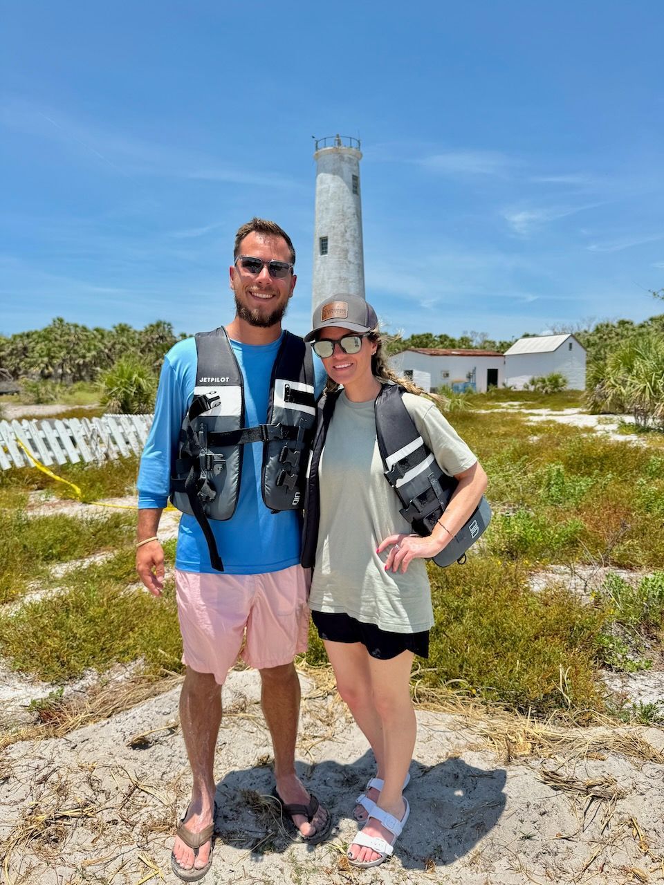 Two people in life vests pose in front of a lighthouse.