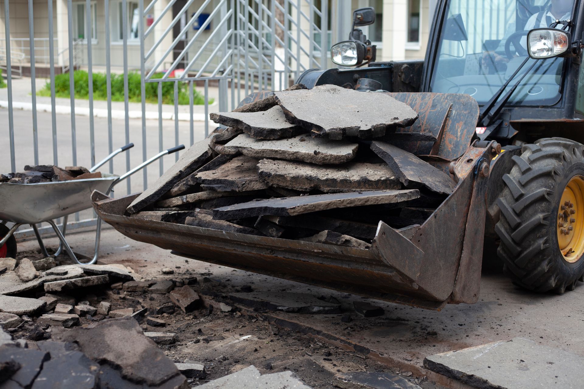 A bulldozer is carrying a pile of concrete in its bucket.