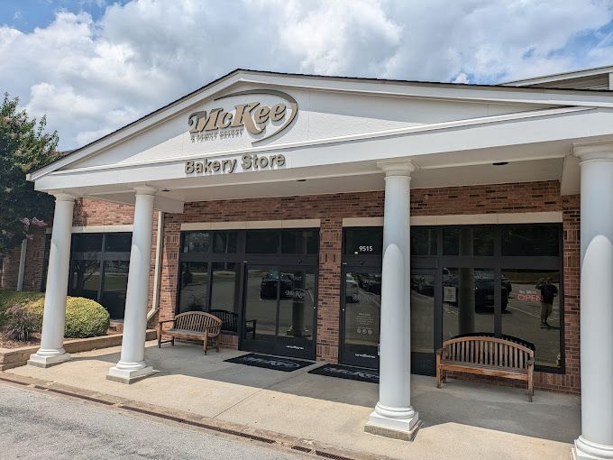 The front of a bakery store with columns and a bench in front of it.