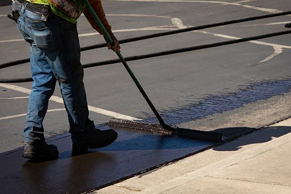Worker Using a Sealcoating Brush During Asphalt Resurfacing — Haverstraw, NY — K & P Asphalt Inc