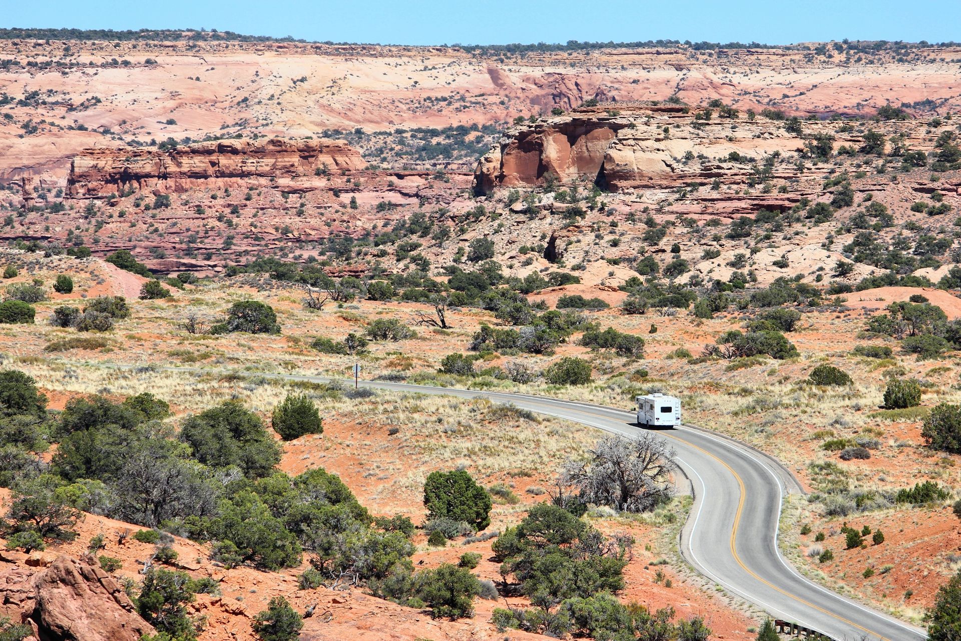 A white rv is driving down a desert road