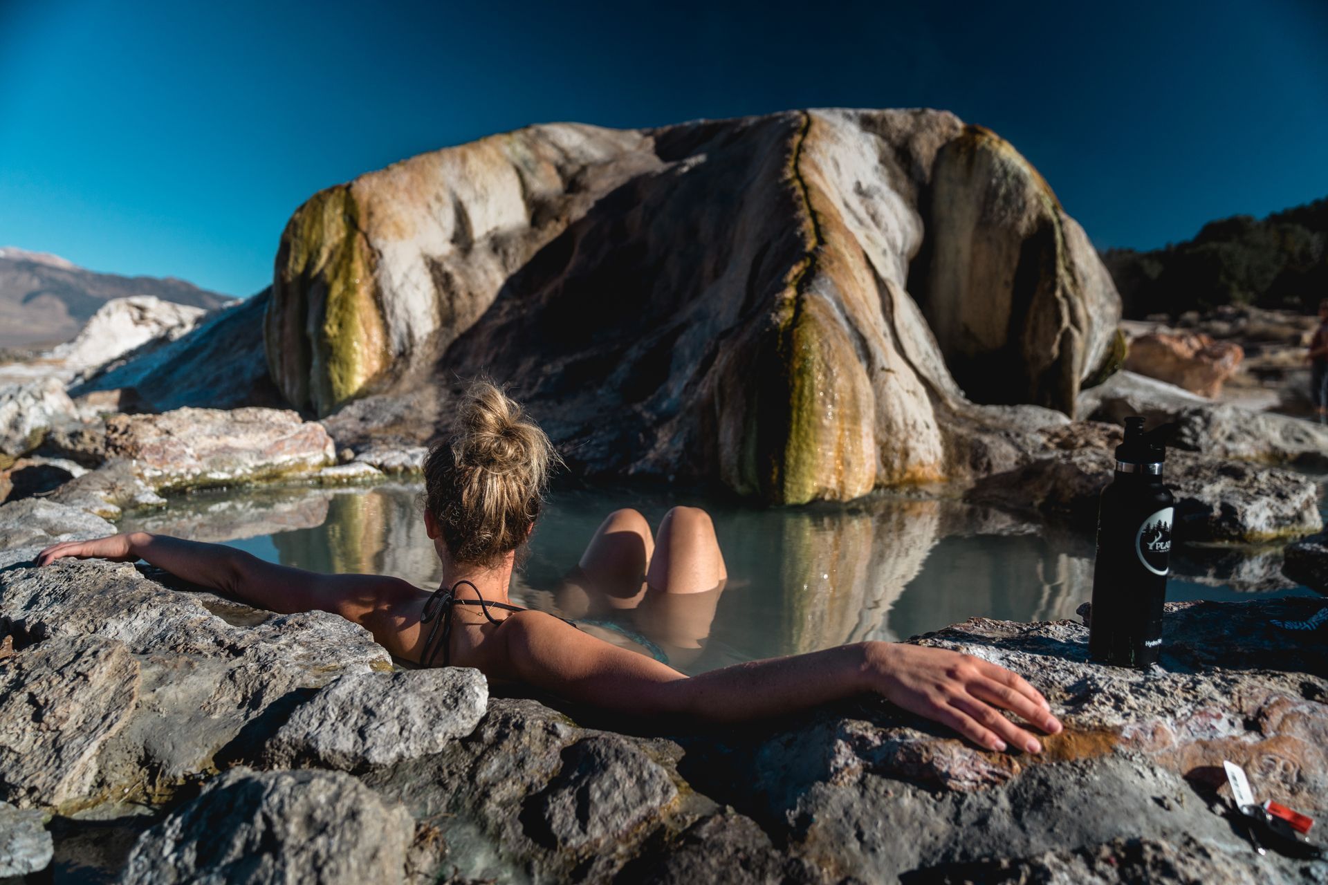 A woman is laying in a hot spring surrounded by rocks.