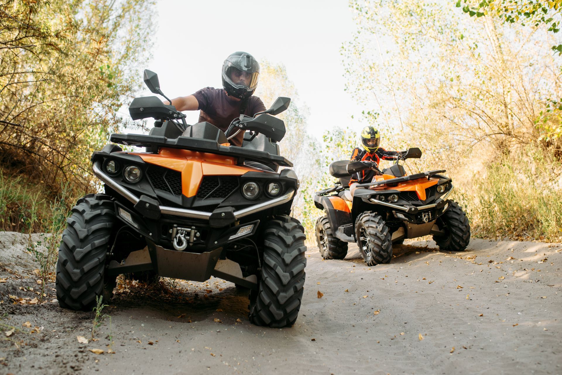 Two people are riding atvs down a dirt road.