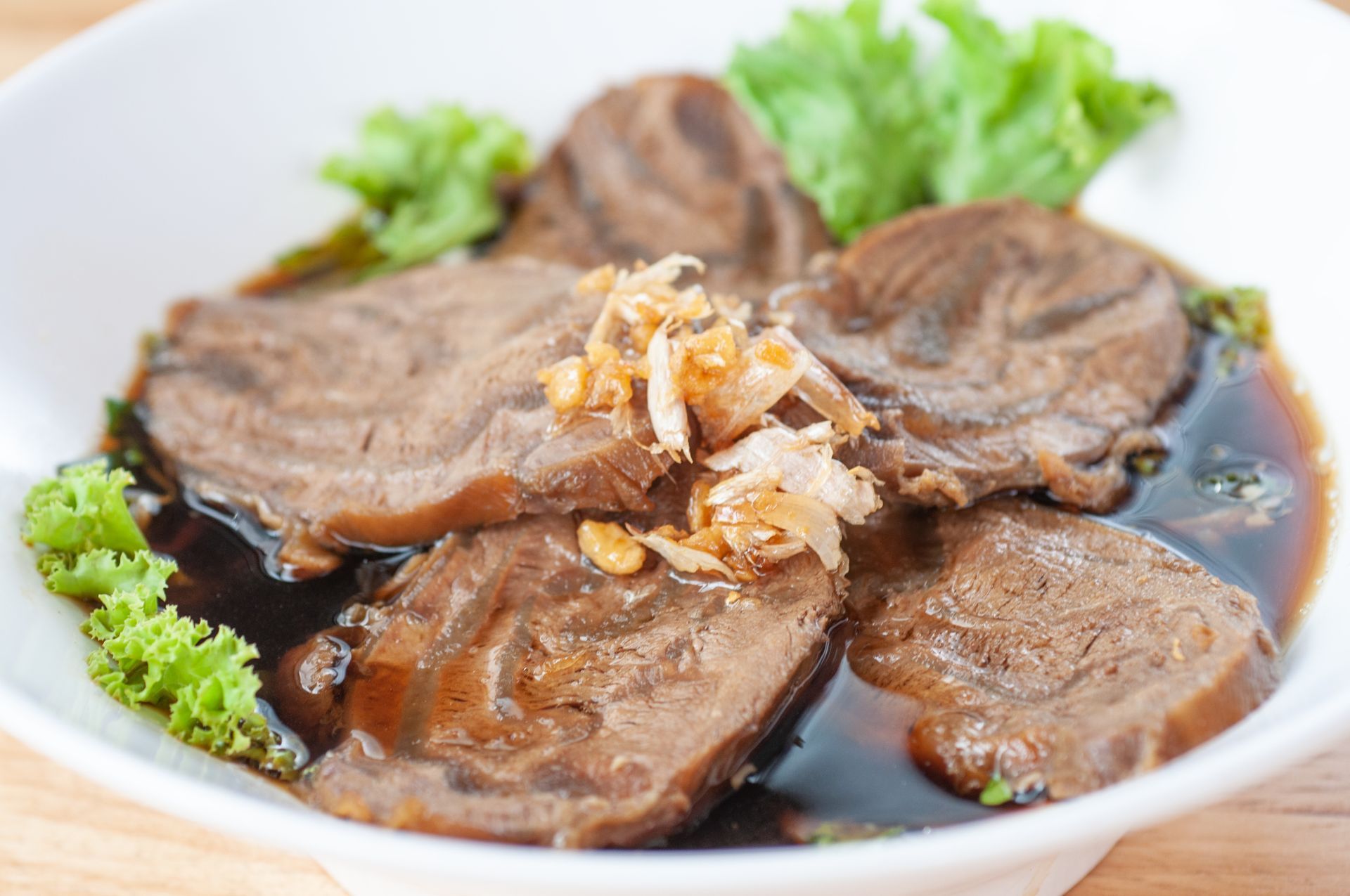 A white bowl filled with meat and sauce on a table.