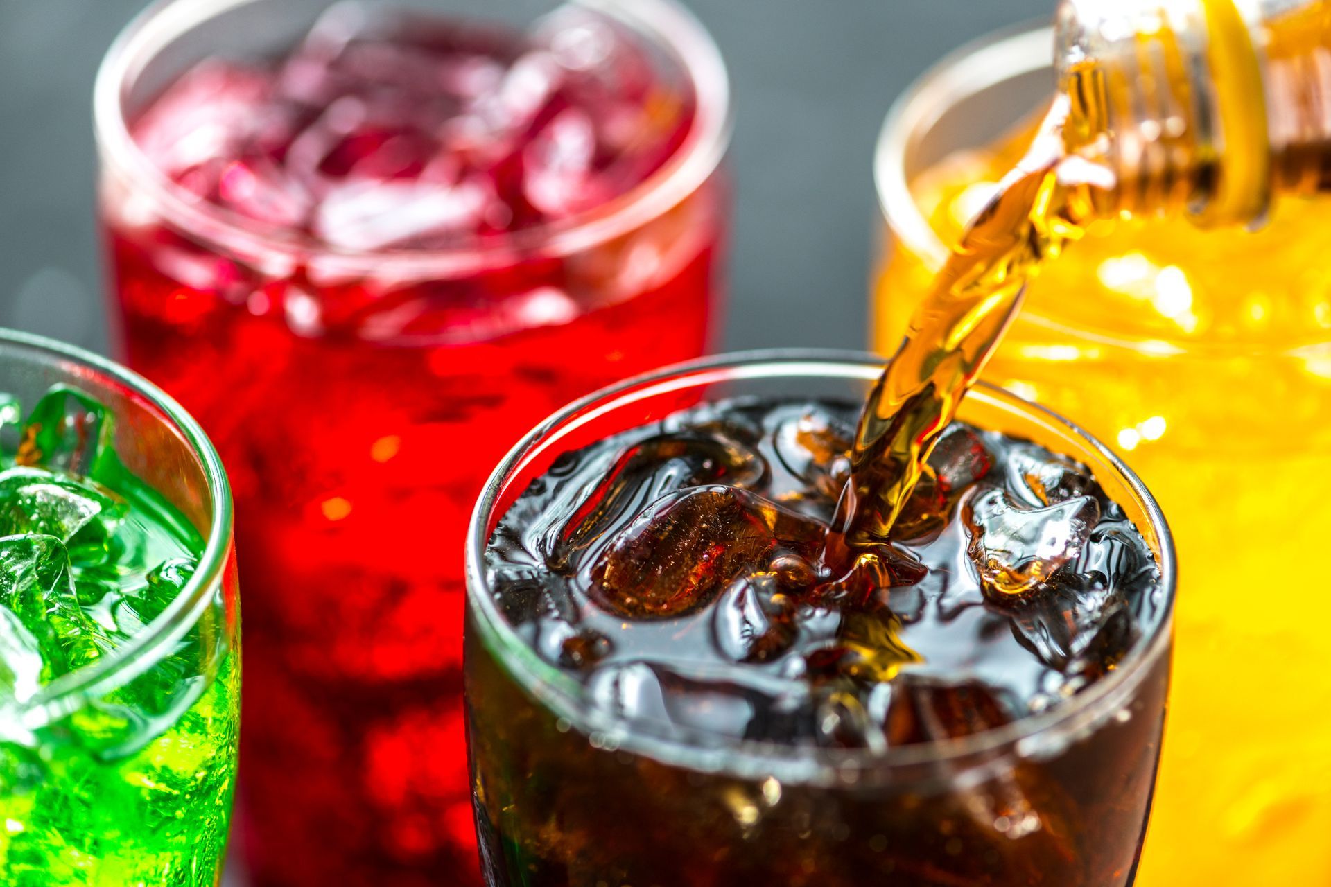 A bottle of soda is being poured into a glass with ice.