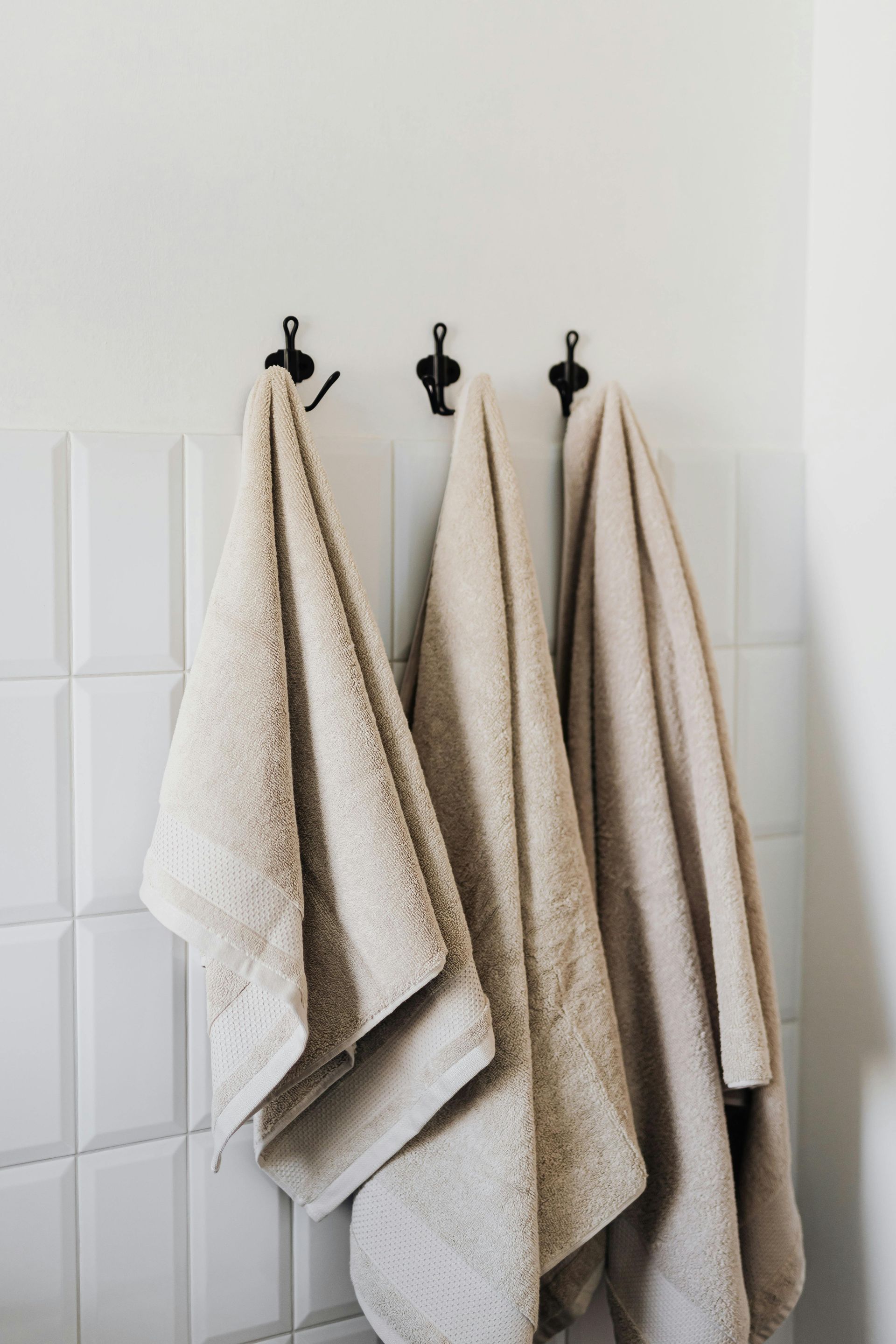 Three towels are hanging on hooks on a wall in a bathroom.