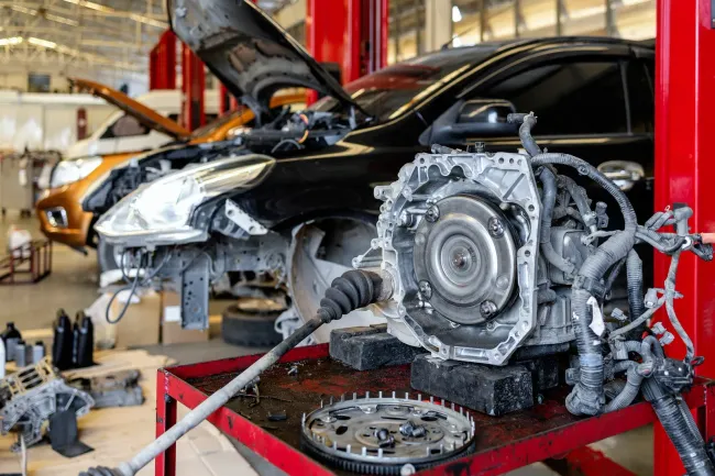 Car workshop with a black car and a removed transmission on a red lift, repairs in progress