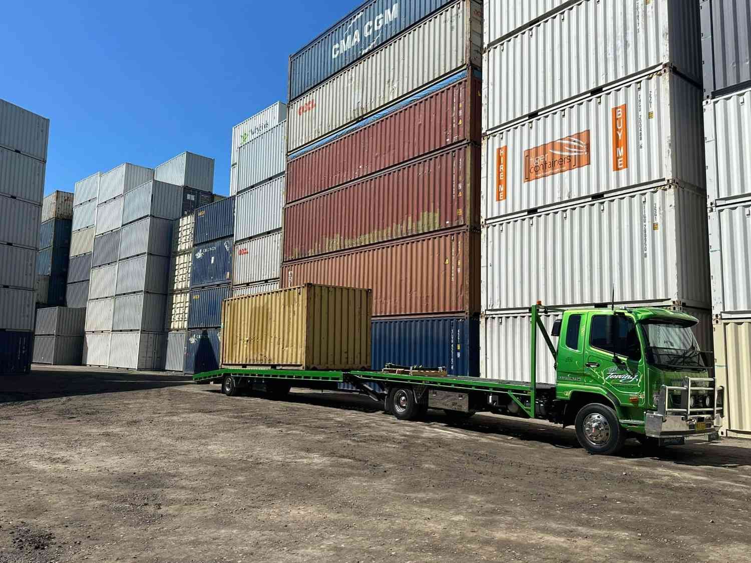 Green Flatbed Truck Carrying a Shipping Container in A Storage Yard — New England Towing in Warialda, NSW