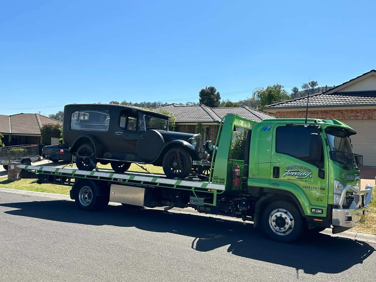 A Green Tow Truck Carrying a Vintage Black Car Parked on A Residential Street — New England Towing in Warialda, NSW