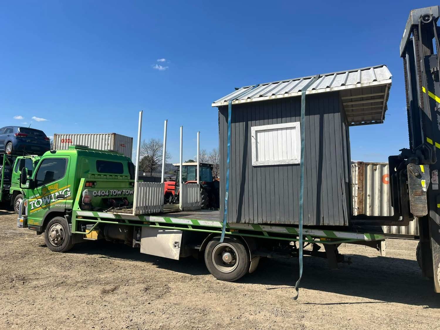 A Green Flatbed Truck Carrying a Small, Gray Shed with A White-Framed Window — New England Towing in Inverell, NSW