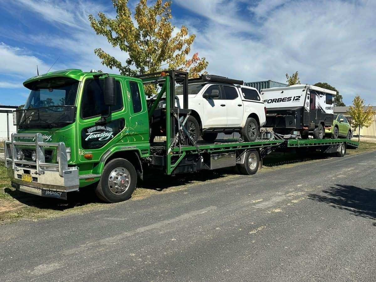 Green Truck Carrying a White Pickup Truck and A Caravan — New England Towing in Ebor, NSW