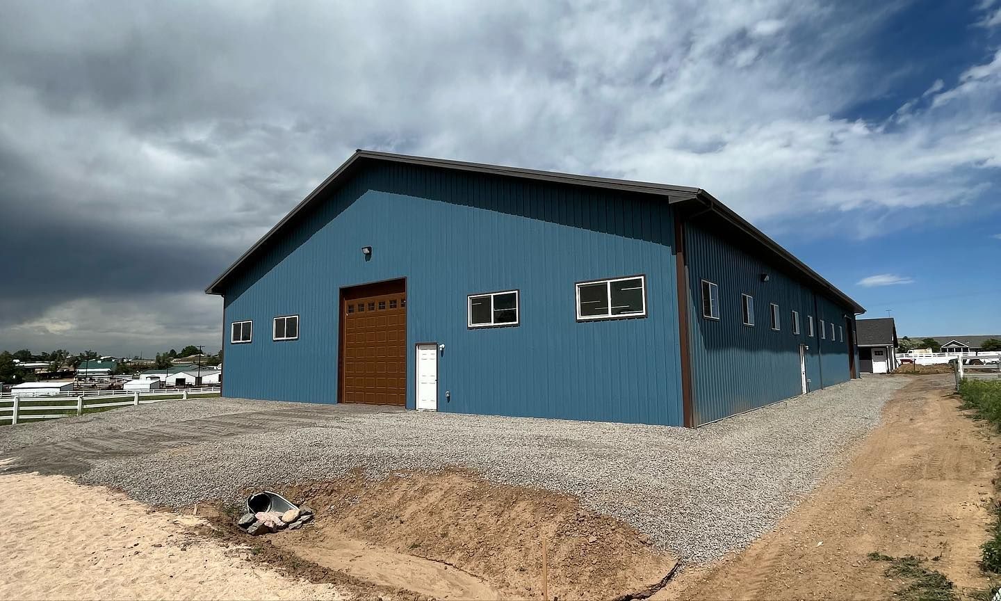 A large blue building with a brown door is sitting on top of a gravel lot.