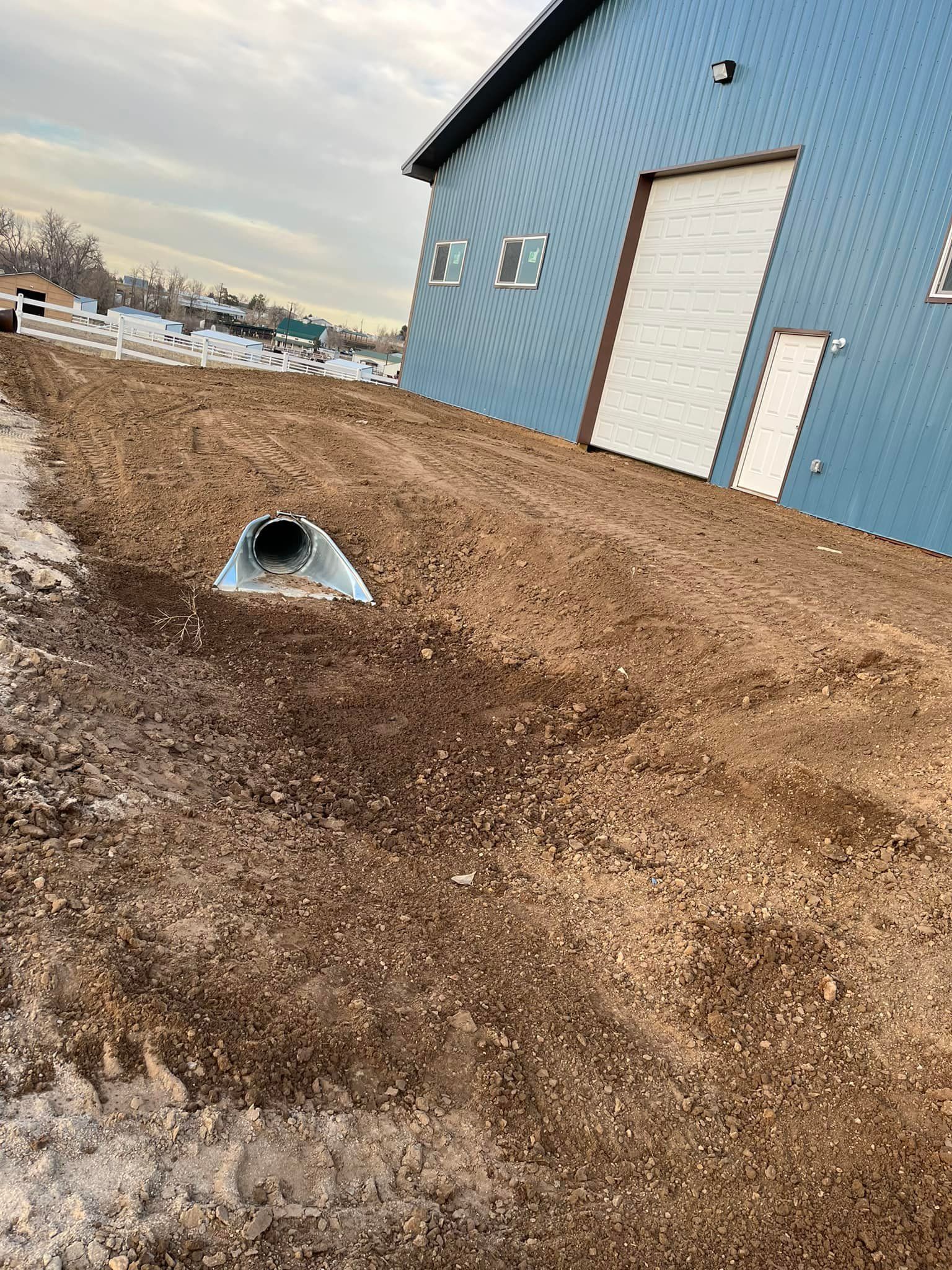 A blue building with a white door is sitting next to a dirt field.