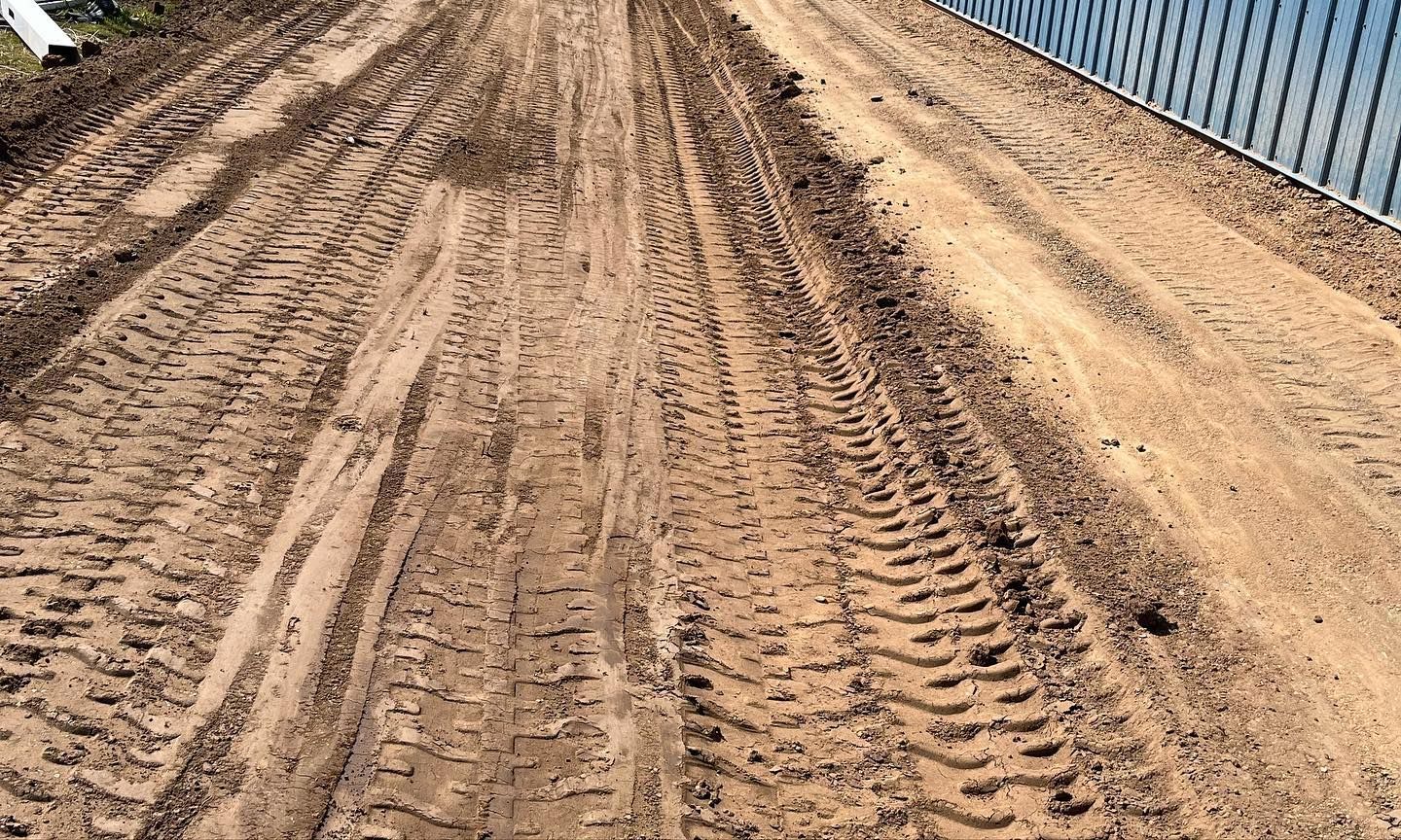 A dirt road with tire tracks on it and a fence in the background.