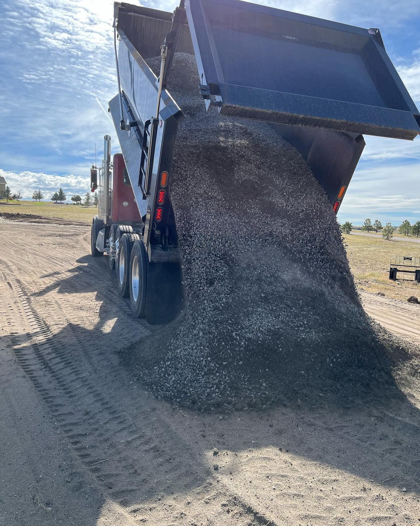 A dump truck is loading gravel into the back of it.