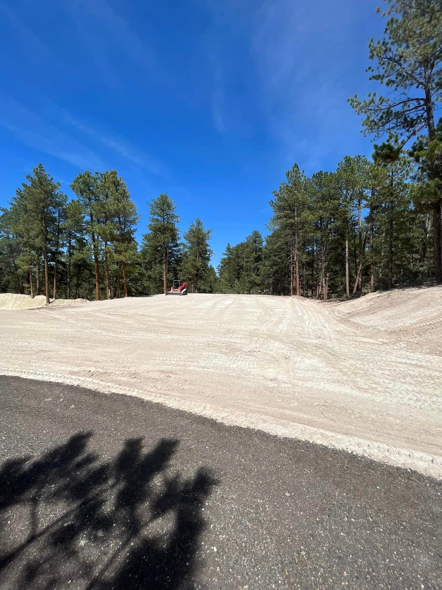 A person is riding a bike down a dirt road with trees in the background.
