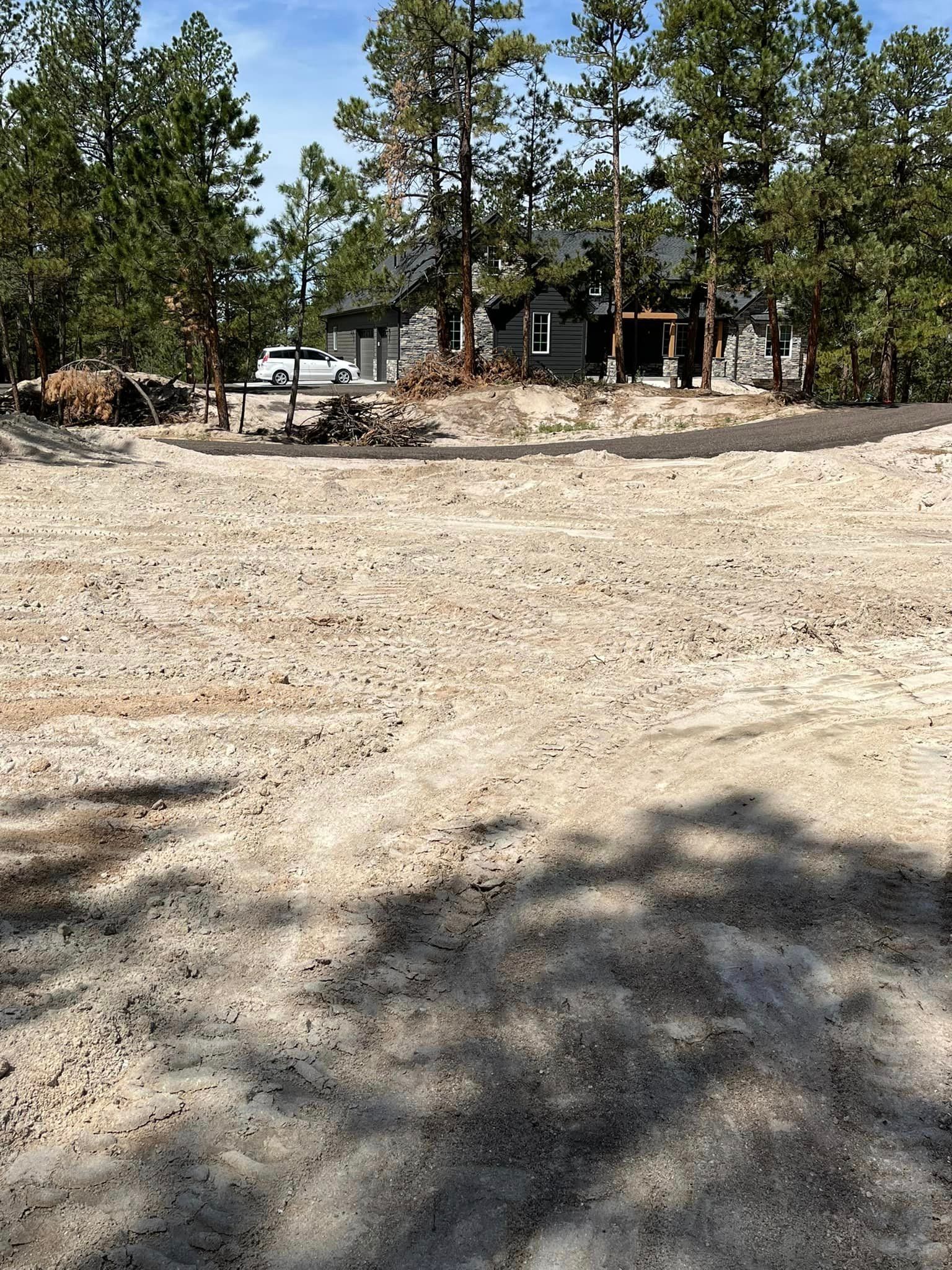 A dirt field with trees in the background and a house in the background.