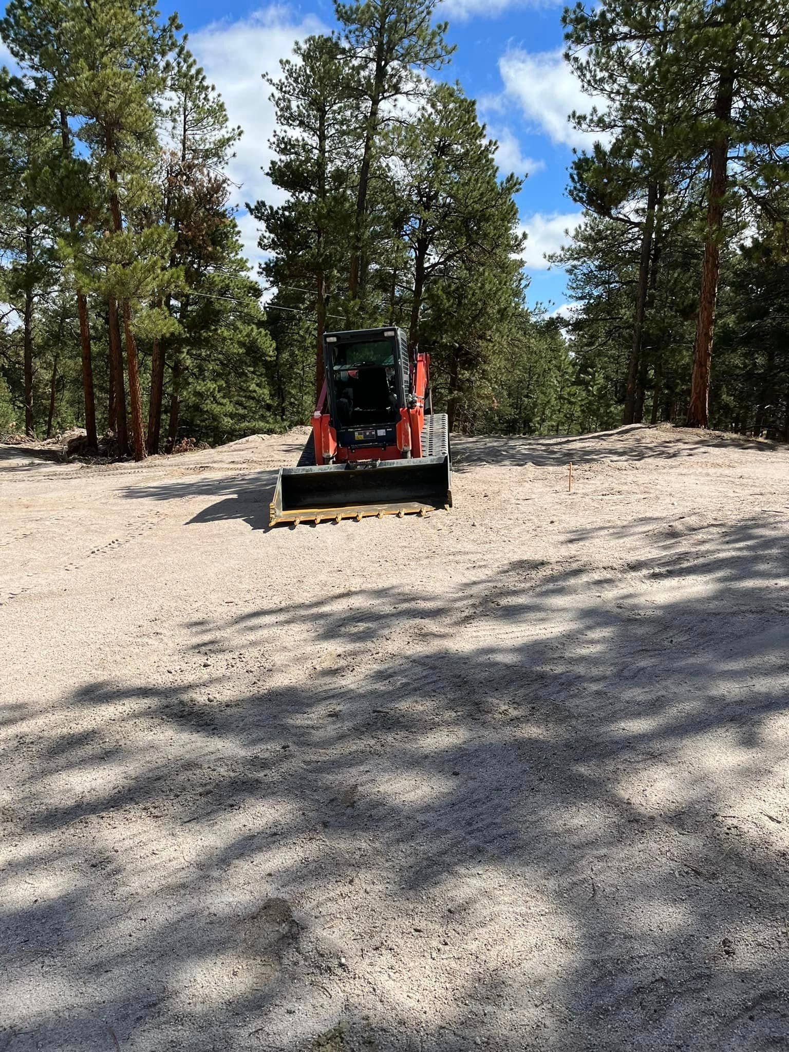 A bulldozer is driving through a dirt field with trees in the background.