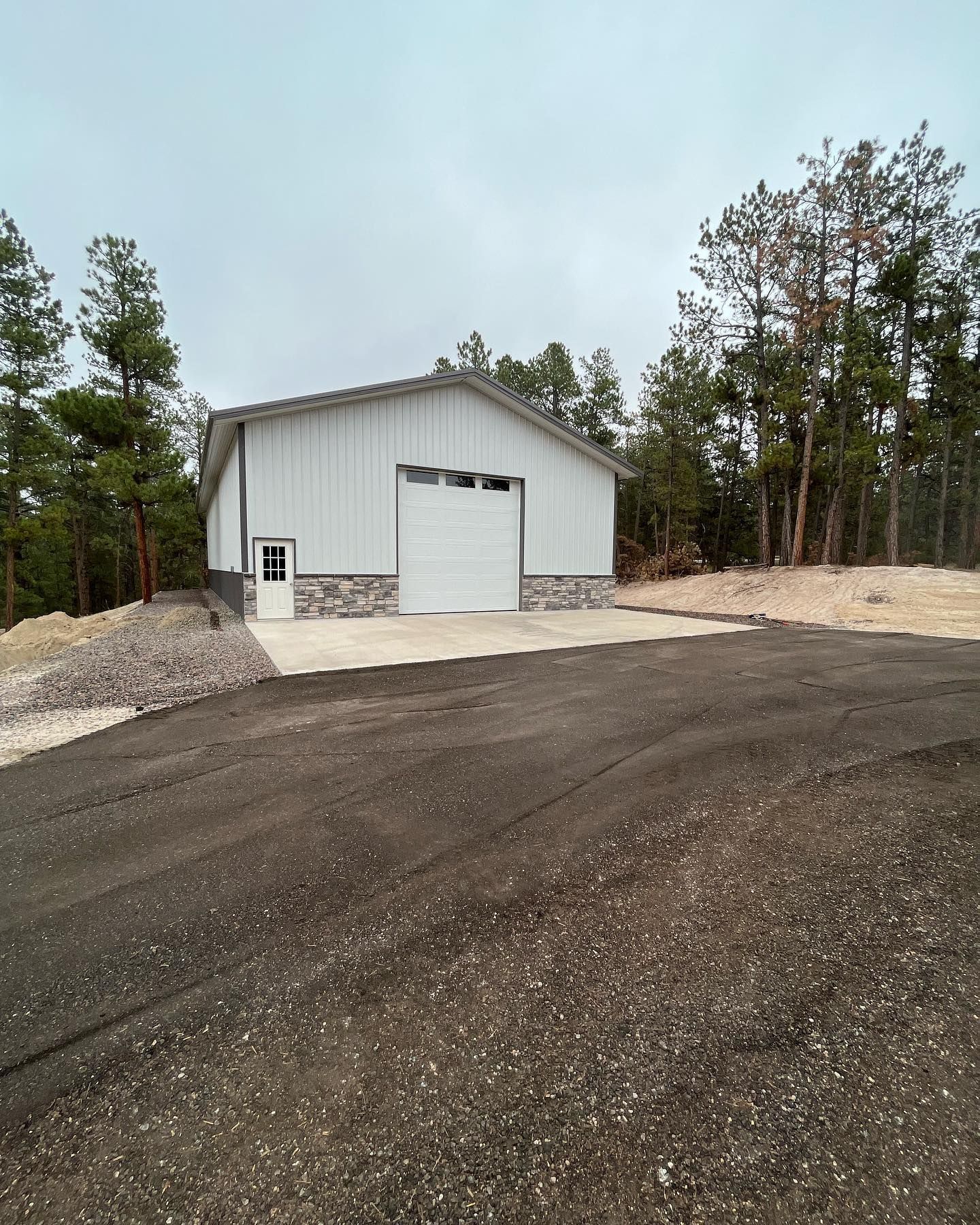 A white building with a garage door is sitting on top of a dirt hill.