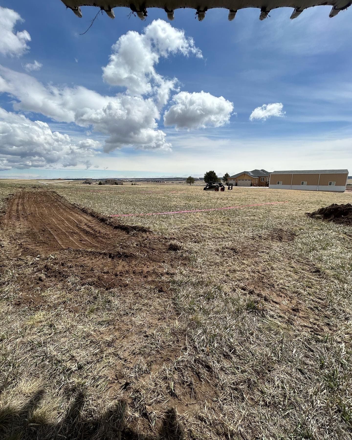 A tractor is plowing a field with a building in the background.