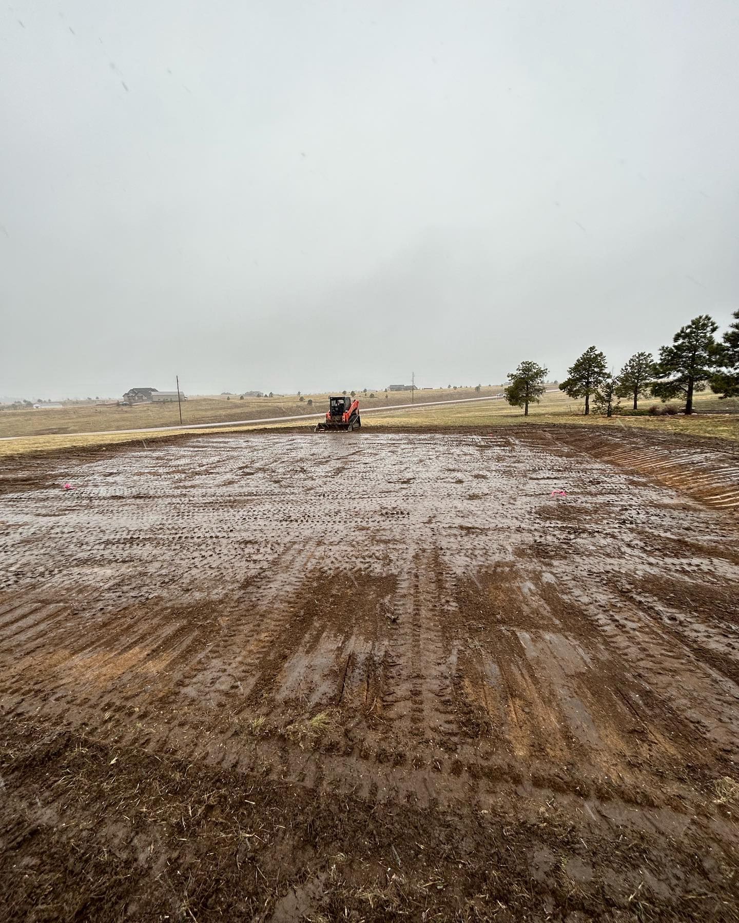 A tractor is plowing a muddy field on a cloudy day.