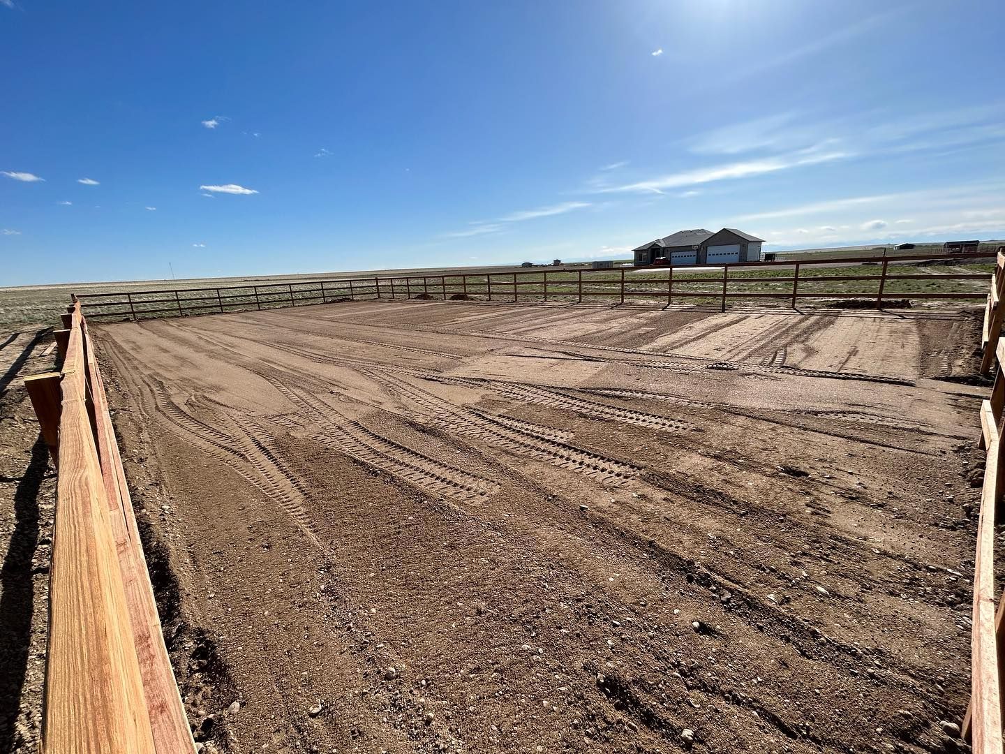 A wooden fence surrounds a dirt field with a house in the background.