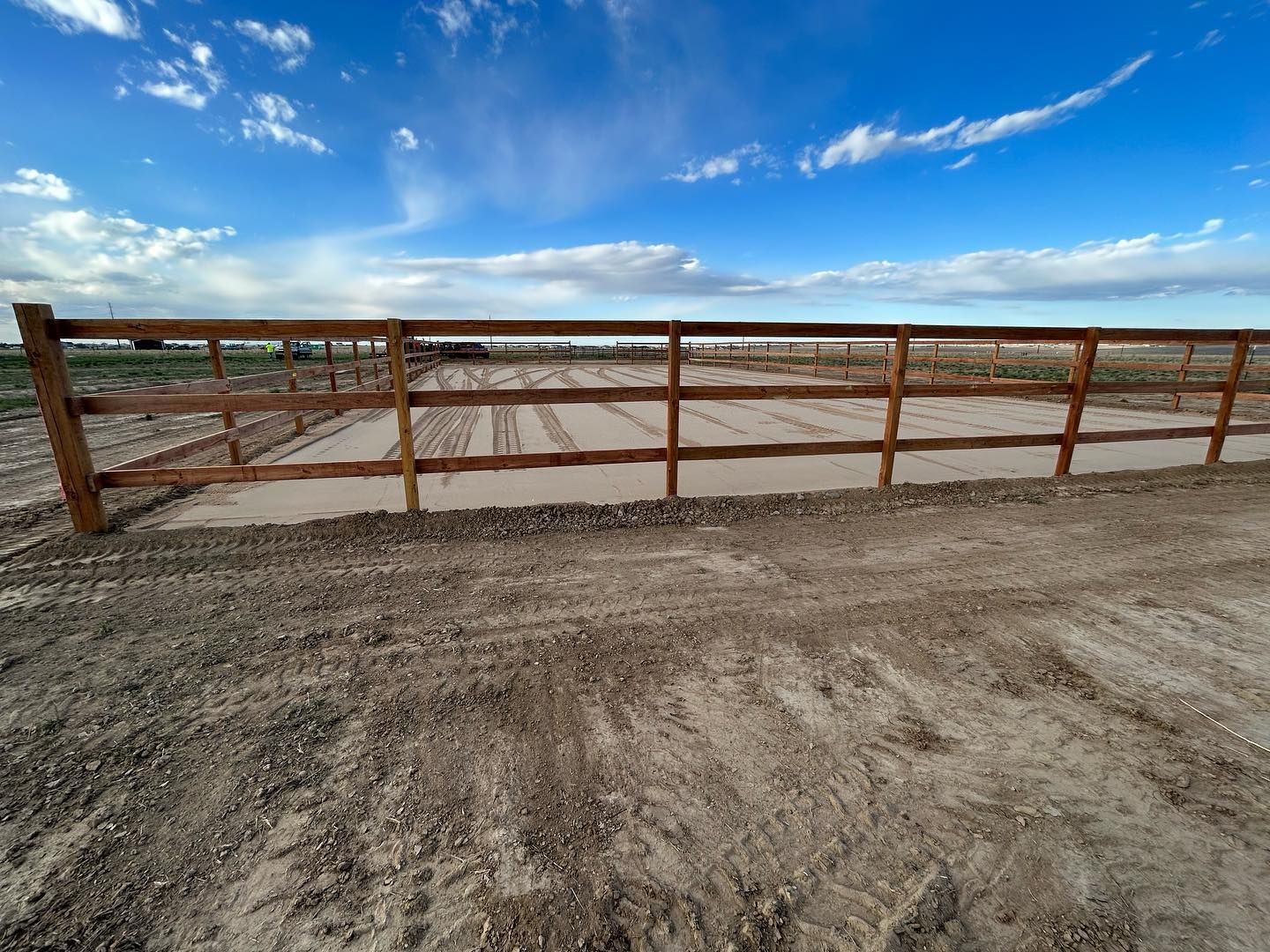 A wooden fence surrounds a dirt field with a blue sky in the background.