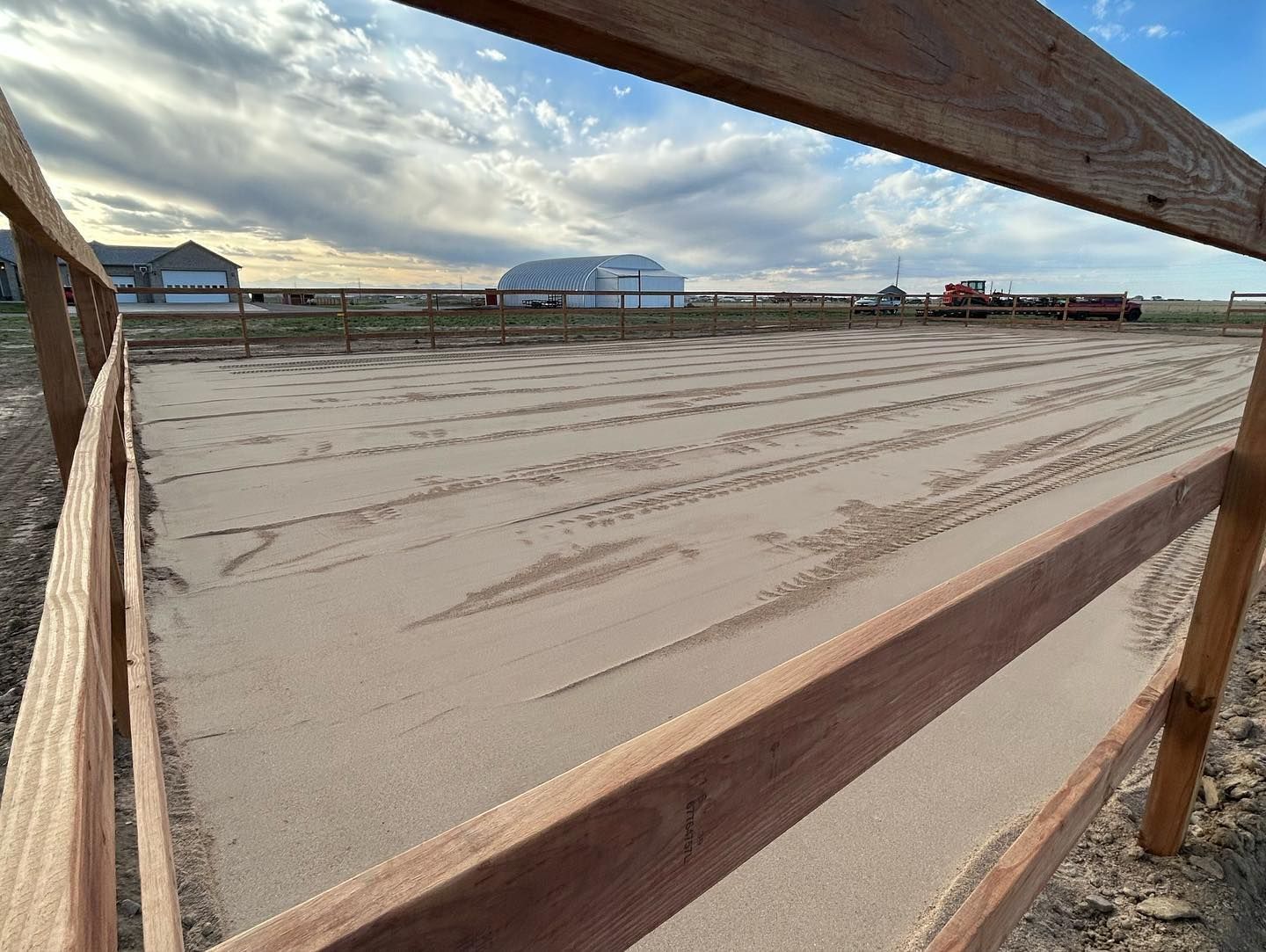 A wooden fence surrounds a dirt field with a building in the background.