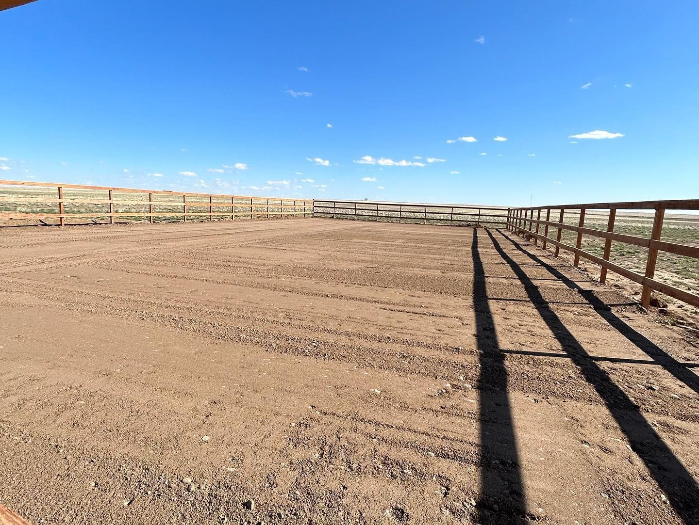 A person is standing in a dirt field with a fence in the background.