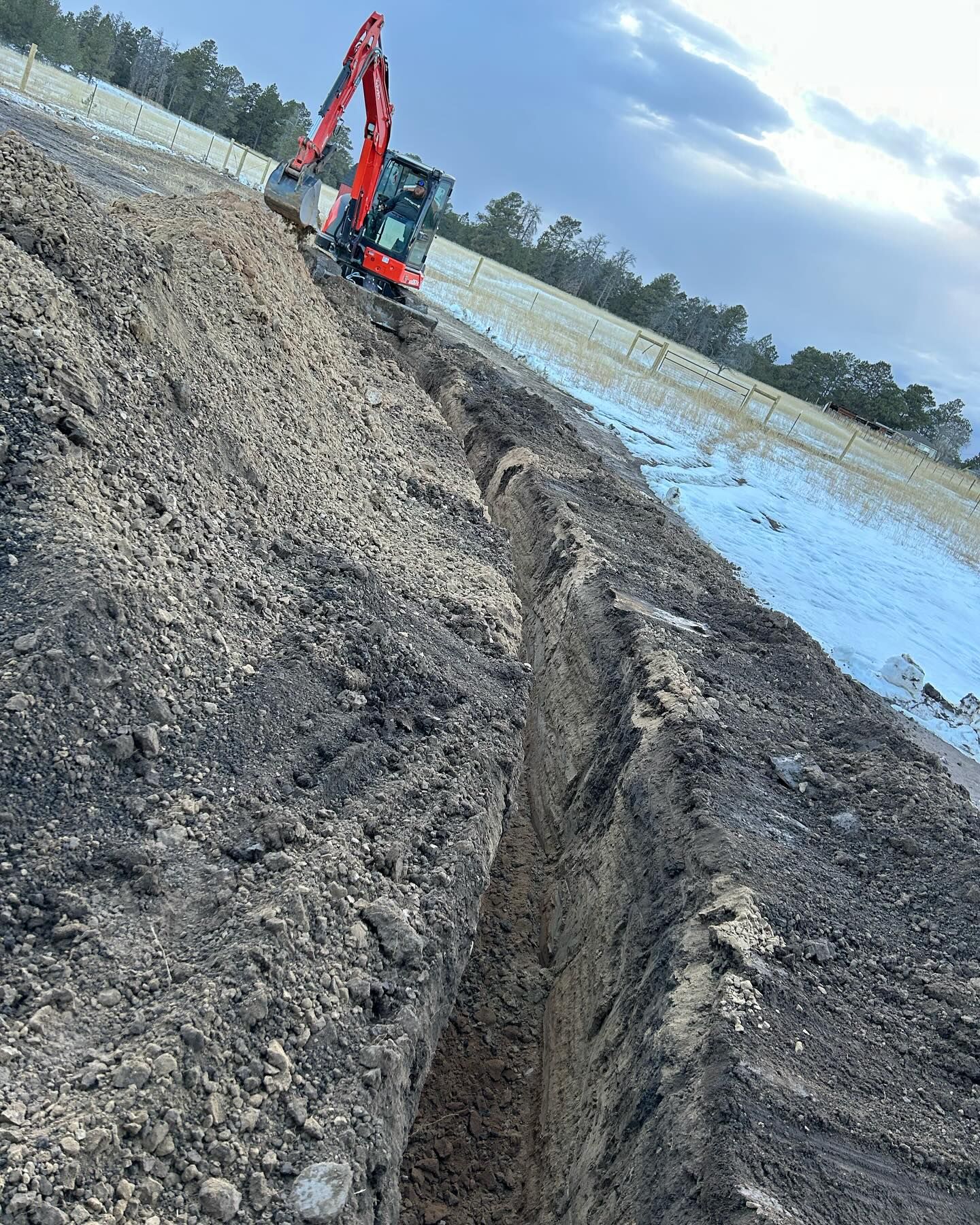 A red and black excavator is digging a trench in the dirt.