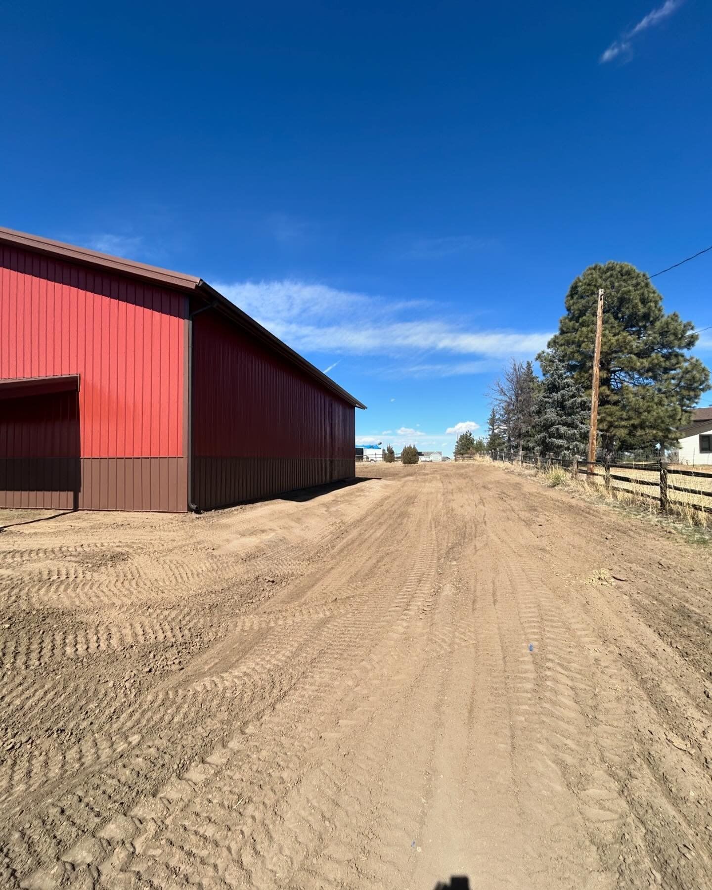 A dirt road leading to a red barn on a sunny day.